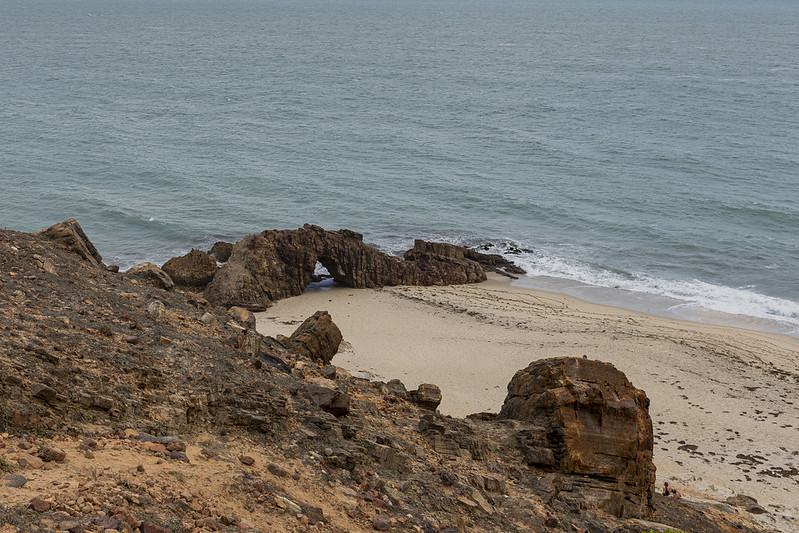 Estrutura de pedras na areia da praia, com um furo no meio, e entrando para o mar, conhecida como Pedra Furada, em Jericoacoara