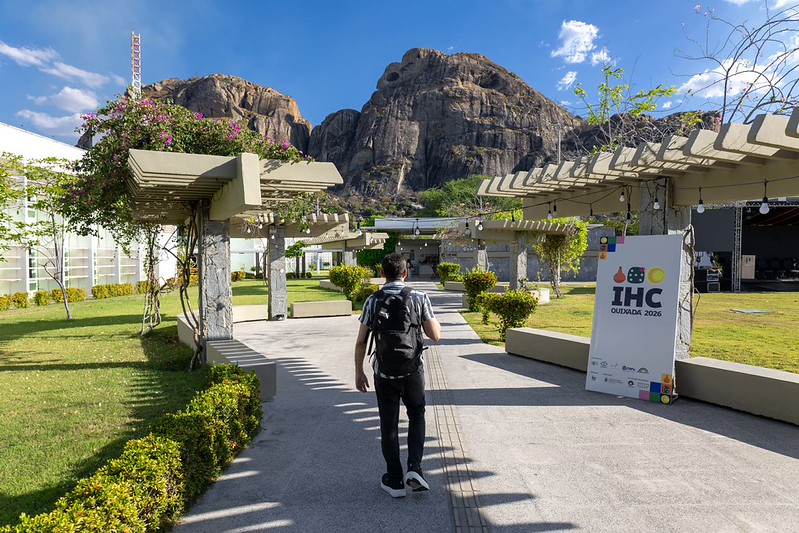 Entrada do Campus de Quixad&aacute;, com uma pessoa passando ao lado do p&ocirc;ster do evento