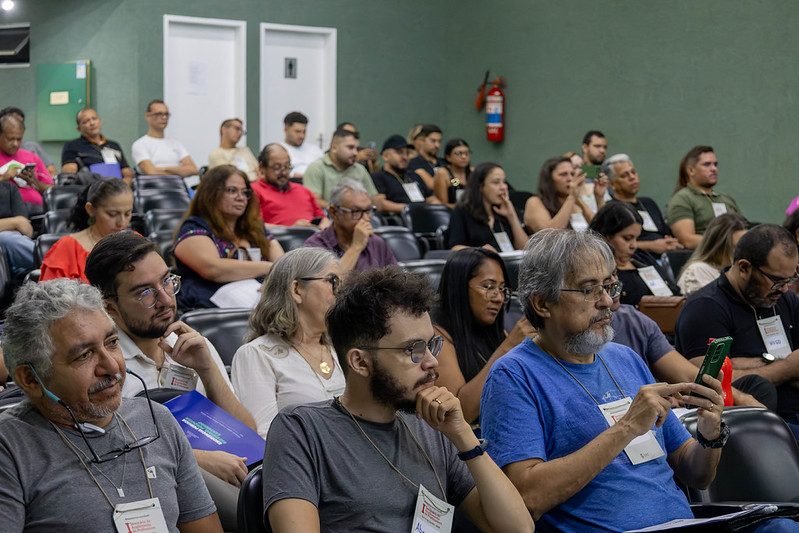 Pessoas sentadas no Auditório Reitor Ícaro de Sousa Moreira acompanham a programação do Seminário de Acolhimento de Professores do Programa Mais Ciência na Escola – UFC. Os participantes observam a apresentação, enquanto alguns fazem anotaçõe