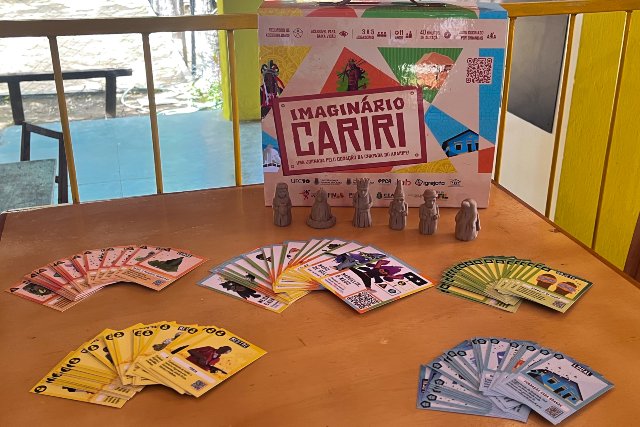 Jogo educativo "Imaginário Cariri": caixa ilustrada, cartas coloridas em leque e peças de madeira sobre a mesa.