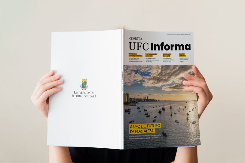 Imagem mostra duas m&atilde;os segurando a Revista UFC Informa, aberta. A capa da revista tem uma foto do por do sol na orla de Fortaleza e os dizeres: "A UFC e o futuro de Fortaleza"