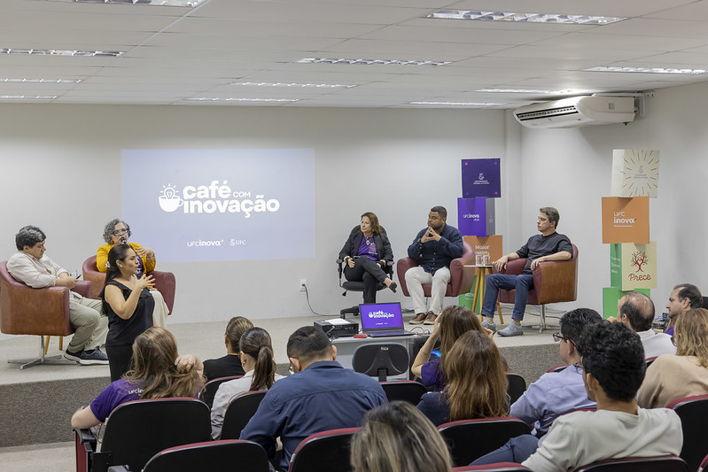Quatro palestrantes e uma mediadora debatem no evento “Café com Inovação”, acompanhados por uma intérprete de Libras.