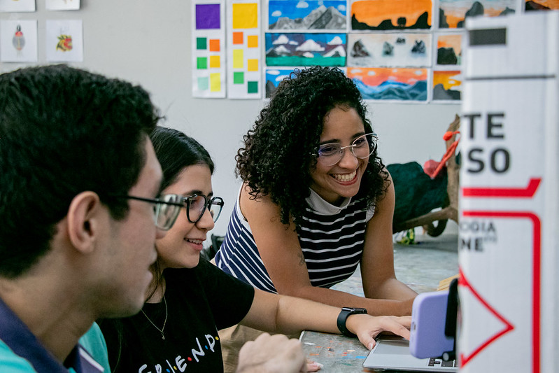 Tr&ecirc;s estudantes de frente para computador em laborat&oacute;rio de inform&aacute;tica