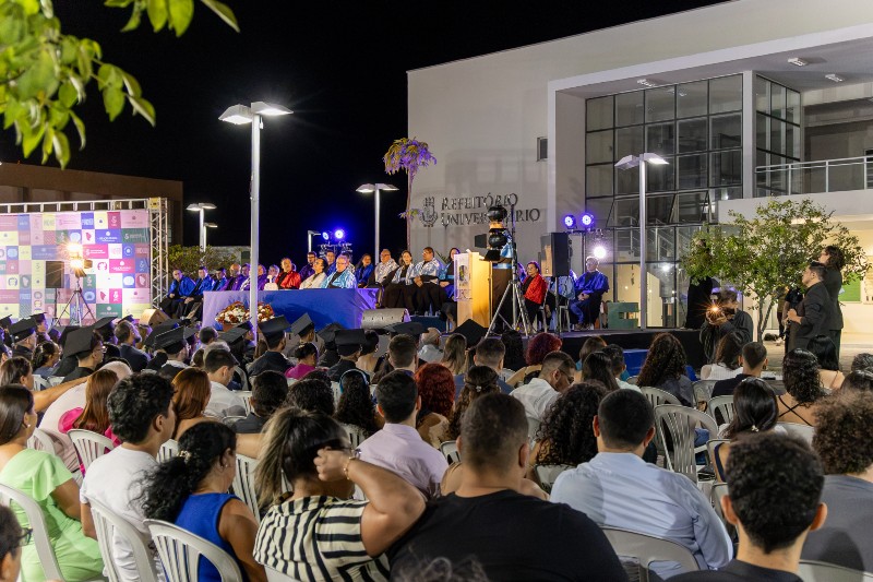 Colação de grau da UFC em Sobral, realizada à noite. Formandos acompanham a cerimônia diante do palco, onde professores e autoridades acadêmicas participam da celebração.