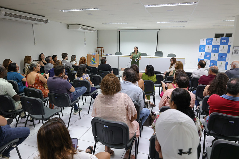 Em audit&oacute;rio, pessoas sentadas ouvem mulher falando ao microfone