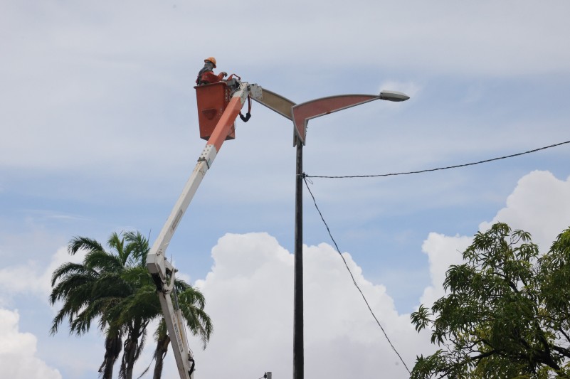 A imagem mostra um homem fazendo a troca de uma l&acirc;mpada de poste
