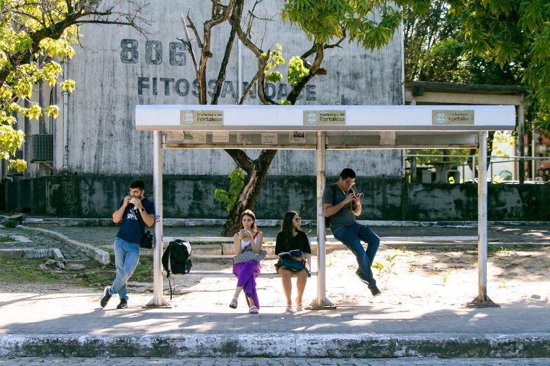 Pessoas parada de ônibus em frente a um prédio do campus do Pici num dia de sol