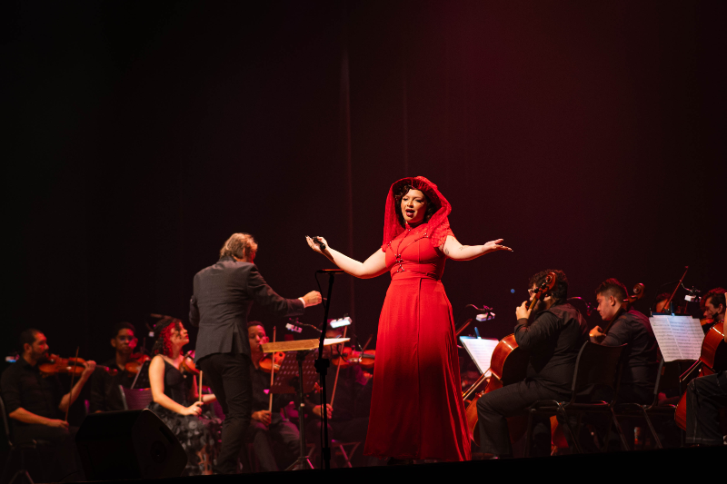 Cantora se apresenta em vestido vermelho, acompanhada por uma orquestra, durante espet&aacute;culo em palco