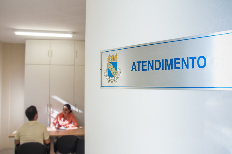 Sala com a placa atendimento, com uma profissional de psicologia e um estudante de costas, com imagem desfocada