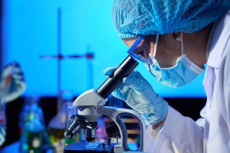 Pesquisadora olha em microscópio dentro de laboratório