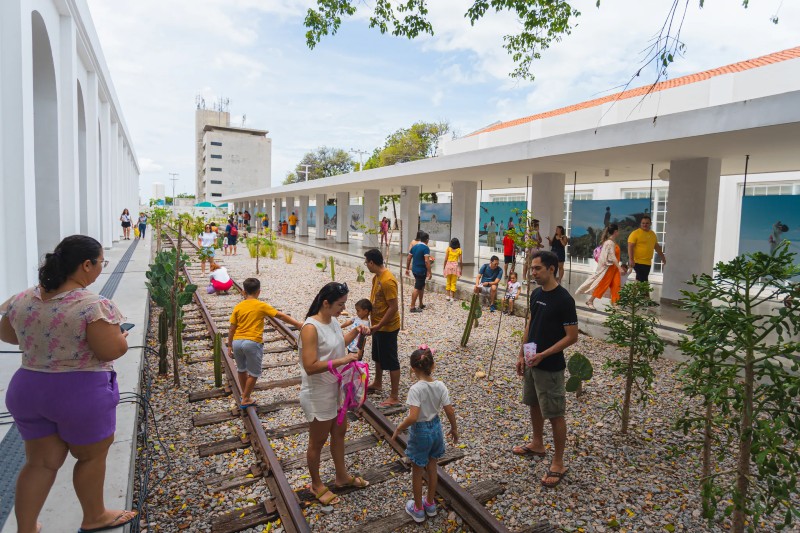 A Esta&ccedil;&atilde;o das Artes &eacute; retratada como um espa&ccedil;o de conviv&ecirc;ncia e cultura, com trilhos ferrovi&aacute;rios, &aacute;reas ajardinadas e arquitetura moderna, onde visitantes de diferentes idades circulam e aproveitam o ambiente ao ar livre