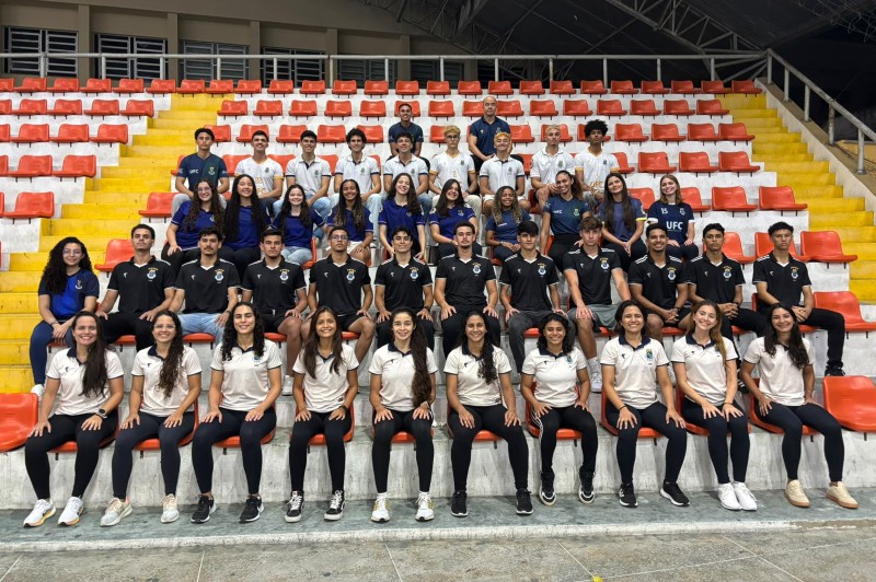 Em uma arquibancada com bancos na cor laranja, 43 jovens est&atilde;o sentados olhando para a foto. Eles ocupam cinco fileiras da arquibancada.