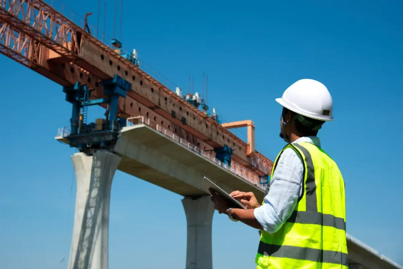 Engenheiro com capacete branco e colete amarelo observa obra de ponte
