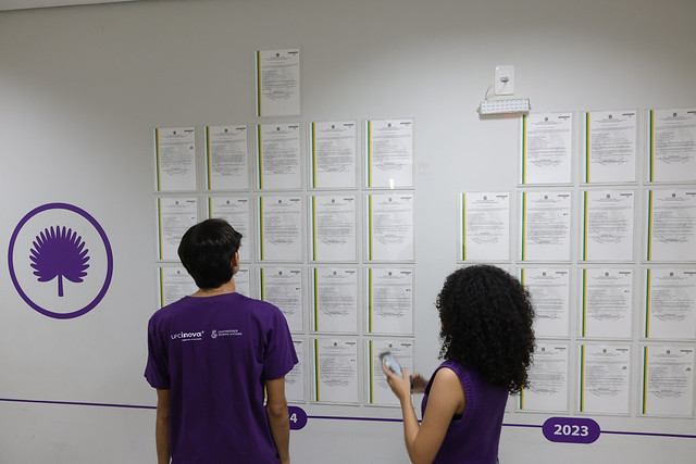 Dois jovens observando mural com as cartas-patente concedidas à UFC