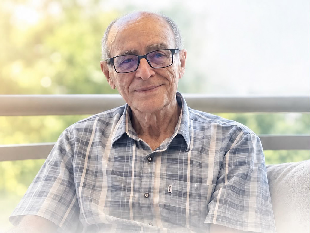 Foto de Francisco Alcides, um homem idoso, de óculos de grau, vestindo blusa com estampa xadrez